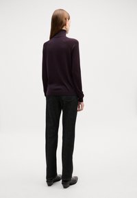 Un pull col roulé violet foncé associé à un jean noir à jambe droite. Les jeans possèdent des poches standards, et le modèle porte des chaussures noires.