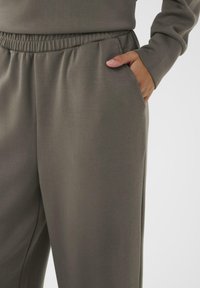 Person wearing dark gray sweatpants with elastic waistband and hand in right pocket against a plain light background.