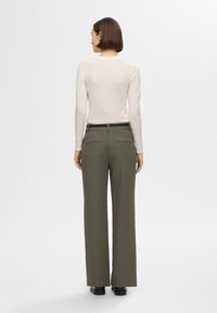 Valge pikkade varrukatega pluus, millele on lisatud kõrge vöökohaga laiad oliivrohelised püksid. Pükstel on taga taskud ning sirge lõige.