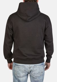 Felpa nera con un ampio cappuccio, polsini e orlo a costine. Realizzata in tessuto morbido, presenta un design semplice senza loghi o motivi. Indossata con jeans in denim chiaro.