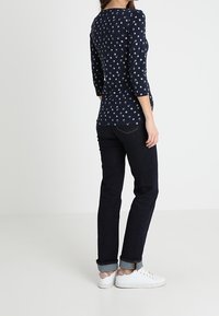 Laivansinis pitkähihaine paita, jossa on pieni kukkakuosi, yhdistettynä tummiin farkkuihin, jotka on käännetty lahkeista, ja valkoisiin lenkkareihin.