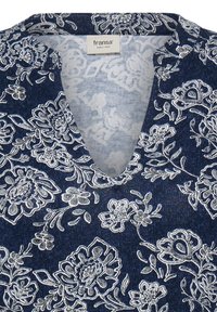 Chemise bleue à motif floral avec des fleurs blanches et des feuilles, avec un col en V et une étiquette en tissu à l'intérieur de l'encolure.