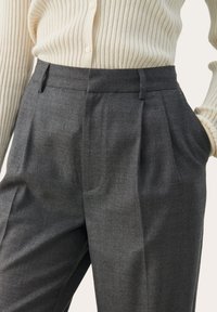 Grijze op maat gemaakte broeken met geplooide voorkant, zijzakken en een gladde stofstructuur, gecombineerd met een crèmekleurige geribde vest.