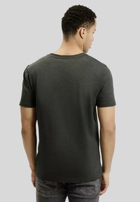 Ciemnozielona koszulka z krótkim rękawem o okrągłym dekolcie, gładka w dotyku i luźno dopasowana, charakteryzująca się prostym i minimalistycznym wzornictwem.