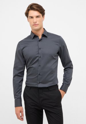 Dunkelgraues Langarmshirt mit Knopfverschluss, Spitzkragen und schwarzen Knöpfen. Glatte Textur, taillierte Passform. Kombiniert mit schwarzen Hosen.