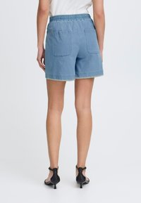 Bermudas de mezclilla en azul claro con una cintura elástica fruncida, dos bolsillos traseros y un borde con forma de concha en el dobladillo.