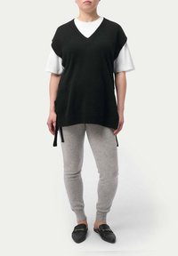 Svart stickad väst med V-ringning, bärs över en vit T-shirt, och matchas med grå leggings och svarta slip-on skor. Västen har sidoförankringar.