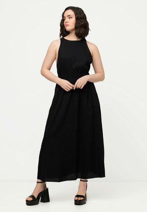 Robe maxi noire avec une coupe sans manches, taille cintrée et jupe fluide. Associée à des sandales à plateforme noires épaisses. Texture lisse.