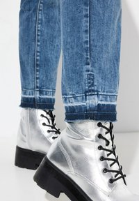 Silver metallic combat boots with black laces and thick black soles, paired with blue distressed denim jeans featuring frayed hems.