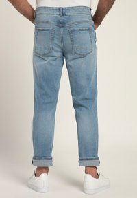 Jeans in denim azzurro chiaro con una vestibilità rilassata, caratterizzati da orli arrotolati, tasche posteriori e dettagli di cucitura sottili. Abbinati a sneakers bianche.