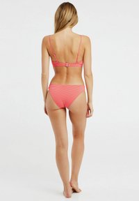 Světle růžový pruhovaný bikiny, které mají top ve stylu bandeau s nastavitelnými ramínky a zapínáním na sponu, doplněné nízko-střiženými bikinovými kalhotkami.