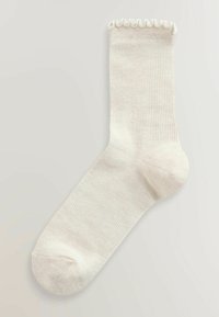 Flødefarvet ribstrømpe med en bølget kant øverst og forstærket hæl og tå. Blødt, tekstureret materiale.