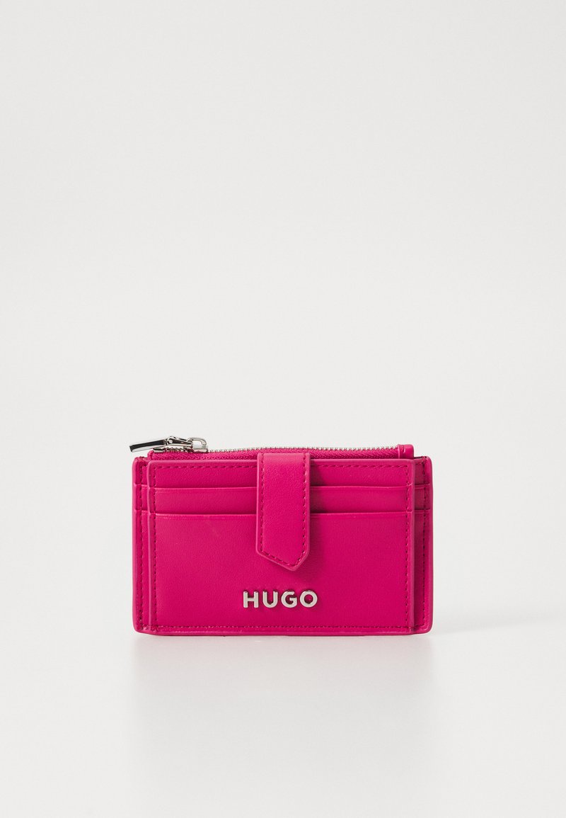 Svetlo roza denarnica iz gladke usnje z zadrgo na vrhu, s številnimi žepi za kartice in srebrnim logotipom "HUGO" na sprednji strani.