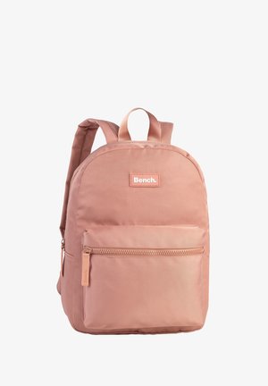 Pink fabric backpack with a rounded shape, featuring a front zip pocket, logo patch, and adjustable straps. Smooth texture throughout.