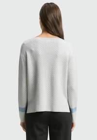 Pull léger gris clair avec un motif texturé, encolure bateau et accents bleus sur les manches. Coupe ample, avec des manches longues et coupe droite.