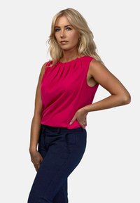 Fuksjowa bezrękawnikowa bluzka z plisowanym dekoltem, połączona z granatowymi spodniami o drobnym wzorze kropek. Gładki materiał i dopasowany krój.