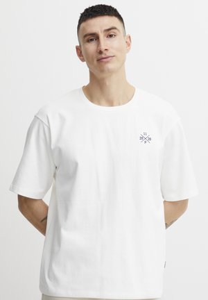 White cotton T-shirt featuring short sleeves and a round neckline. Small navy graphic design on the left chest. Smooth texture.