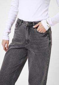 Jeans visokog struka, opuštenog kroja u tamnosivom denimu. Ima pet džepova, rajsferšlus i metalnu dugmad. Tekstulisana tkanina sa blagim sjajem.