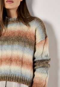 Strickpullover mit einem strukturierten Wellenmuster in sanften Farbabstufungen von Pfirsich, Hellblau und erdigem Braun. Verfügt über einen gerippten Halsausschnitt und Bündchen.