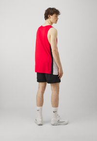Punane varrukateta tank top mustade äärtega, koos mustade sportlike lühikestega. Valged sokid ja tennisetossud. Lihtne disain, kerge kangas.