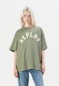 Olijfgroene oversized t-shirt met witte gebogen "REPLAY"-tekst aan de voorkant, rond de ronde halslijn en korte mouwen.