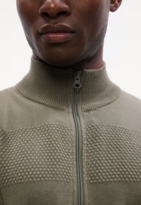 Maglione verde a zip con colletto alto, caratterizzato da trame a nido d'ape testurizzate e un collo e una zip in costa liscia.