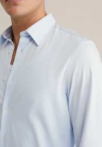 Világoskék, gombos ing hegyes gallérral, sima textúrával, diszkrét fényességgel és fehér gombokkal az elején.