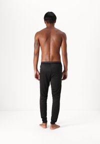 Svarta sportbyxor med en åtsittande design, med ett elastiskt midjeband och avsmalnande ben, sedd bakifrån mot en vit bakgrund.