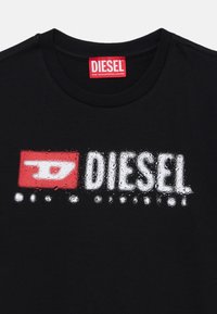 Schwarzes Baumwoll-T-Shirt mit einem großen, abgenutzten weißen und roten "DIESEL"-Logo, rundem Ausschnitt und kurzen Ärmeln.