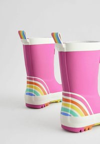 Bottes de pluie en caoutchouc rose avec des accents blancs et des motifs arc-en-ciel sur les côtés. Présentent des tirants colorés à rayures et des semelles texturées.