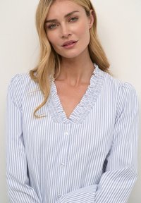 Helles Blau und weiße gestreifte Bluse mit Rüschenschnitt am V-Ausschnitt und Knopfverschluss. Verfügt über lange Ärmel und eine weiche, glatte Stofftextur.