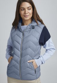 Vest matlasat de culoare albastru deschis, cu glug�ă, dotat cu fermoar frontal, buzunare laterale și accente tricotate de culoare navy pe umeri și mâneci.