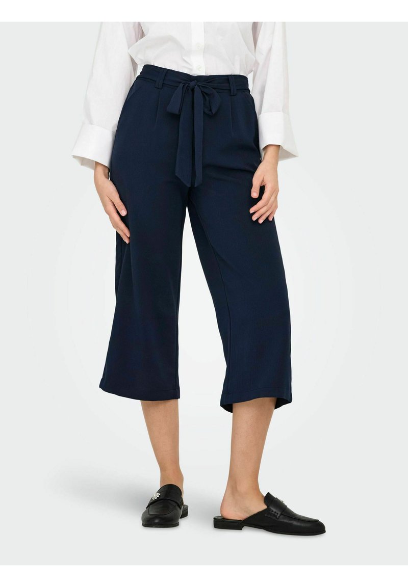 Pantalon culotte bleu marine en tissu léger, avec une taille nouée et une longueur raccourcie. Texture lisse avec une coupe décontractée.