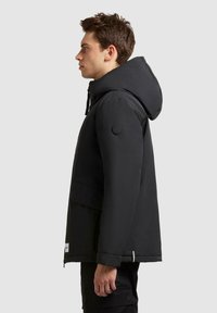 Schwarze isolierte Jacke mit Kapuze, ausgestattet mit einem Badge am Ärmel, Reißverschluss und einer lässigen Passform, entworfen für Wärme und Komfort.