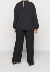 Svart blus med nyckelhållsrygg, långa ärmar och detaljer med pärlor vid kragen. Matchas med svarta vida byxor och svarta klackskor.