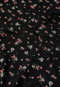 Kukallinen kangas mustalla taustalla, jossa on pieniä punaisia ja valkoisia kukkia vihreillä lehdillä. Materiaali näyttää kevyeltä ja sileältä.