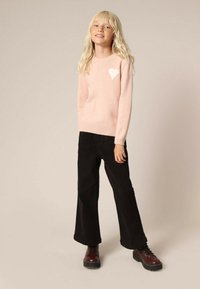 Pull en tricot rose clair avec un motif de cœur blanc, associé à un pantalon évasé noir et des bottes à lacets marron foncé. Texture lisse dans l'ensemble.