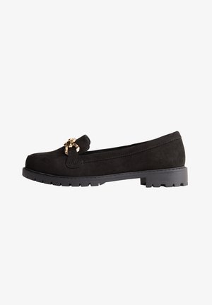 Mocassin en daim noir avec semelle épaisse et accent chaîne dorée sur le dessus, vue latérale sur fond blanc.