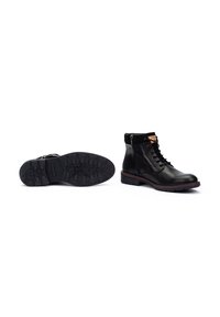 Botas negras de cuero hasta el tobillo con un sistema de cordones en la parte delantera, cremallera lateral, suela texturizada y acentos de costura roja en la suela.