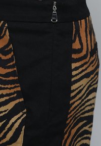 Hnědá a černá sukně se vzorem tygřích pruhů, s uzávěrem na zip, se kontrastním černým bočním panelem a hladkou textilní strukturou.