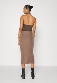 Un top halter marron et une jupe midi en tricot, présentant une texture côtelée. La tenue est associée à des bottines noires.