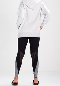 Czarne legginsy z siateczkowymi wstawkami i wzorzystymi panelami, w połączeniu z szarą bluzą z kapturem. Legginsy mają dopasowany krój i długość do kostek.
