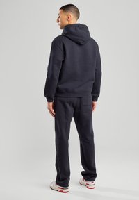 Felpa navy con cappuccio regolabile, polsini a coste e pantaloni coordinati. Tessuto morbido, design minimalista, vista da dietro.