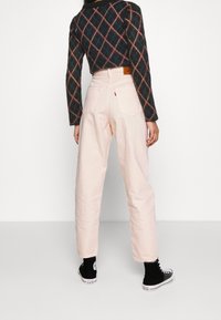 Jeans de talle alto en rosa pálido con un corte recto, combinados con un suéter oscuro de estampado y zapatillas negras. La vista trasera muestra un detalle mínimo.