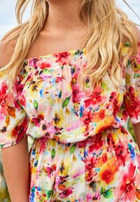 Robe fleurie à épaules dénudées aux motifs vibrants rose, rouge et jaune. Tissu léger et texturé avec une taille élastique.
