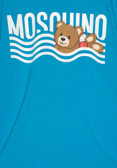 Tyrkysové tričko s grafikou hnedého medveďa, ktorý si oddychuje na červenom bóje so bielymi vlnami a textom "MOSCHINO" nad ním.