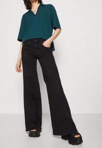 Själsblå oversized ribbad blus med korta ärmar, v-ringning, kombinerad med höga svarta vida jeans och kraftiga svarta sandaler.