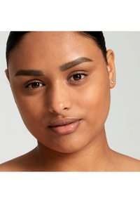 Porträt einer Person mit mittlerem Hautton, klarer Haut, mittelbraunem Haar, definierten Augenbrauen und natürlicher Lippenfarbe, vor einem neutralen Hintergrund.