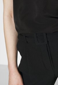 Svart ärmlös topp med en slät textur, kombinerad med högmidjade svarta byxor som har bälte och plissédetaljer.