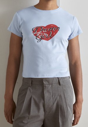 T-shirt corta azzurro chiaro in morbido cotone con maniche corte. Presenta una grafica a cuore rosso con il testo "Damn Girl" in corsivo argento.